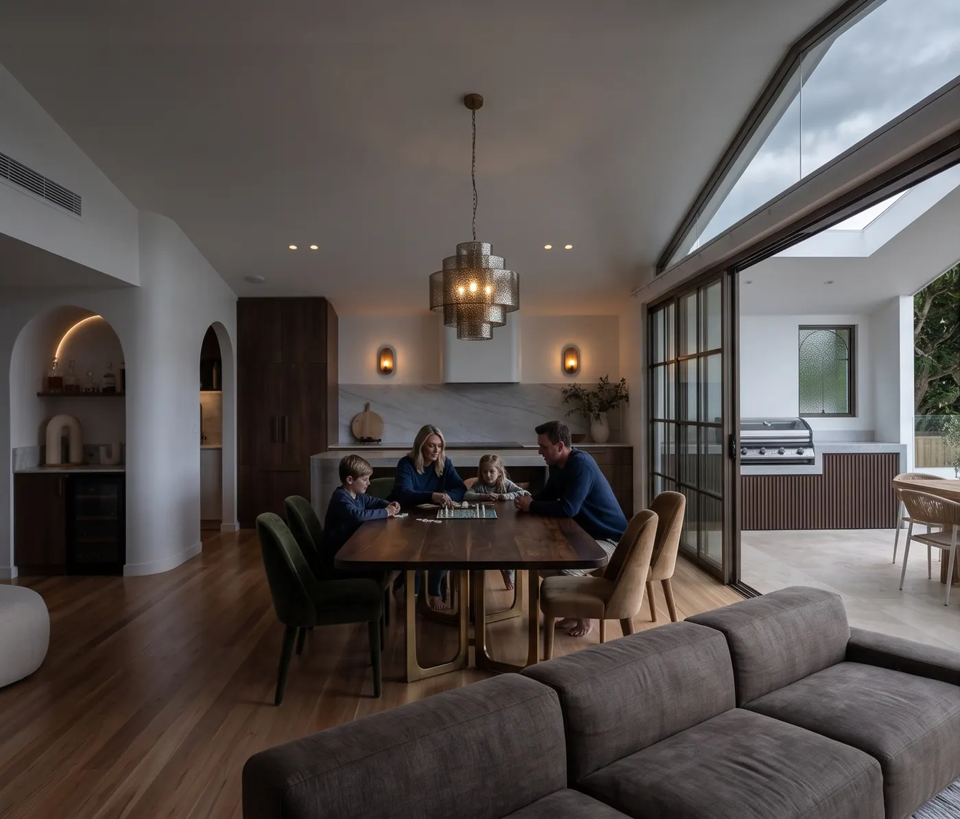 An open plan kitchen, dining and living room whose living areas face south, grey and lit by lamps in the middle of the day